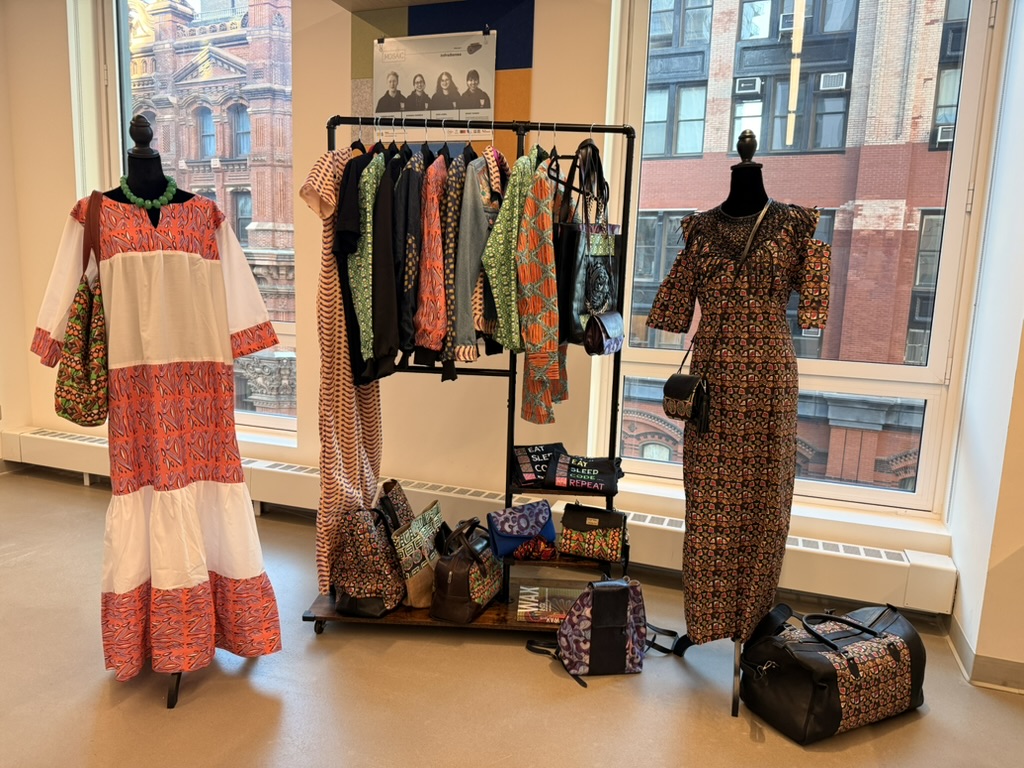 Finished collection on display: dresses on mannequins, a garment rack and printed bags